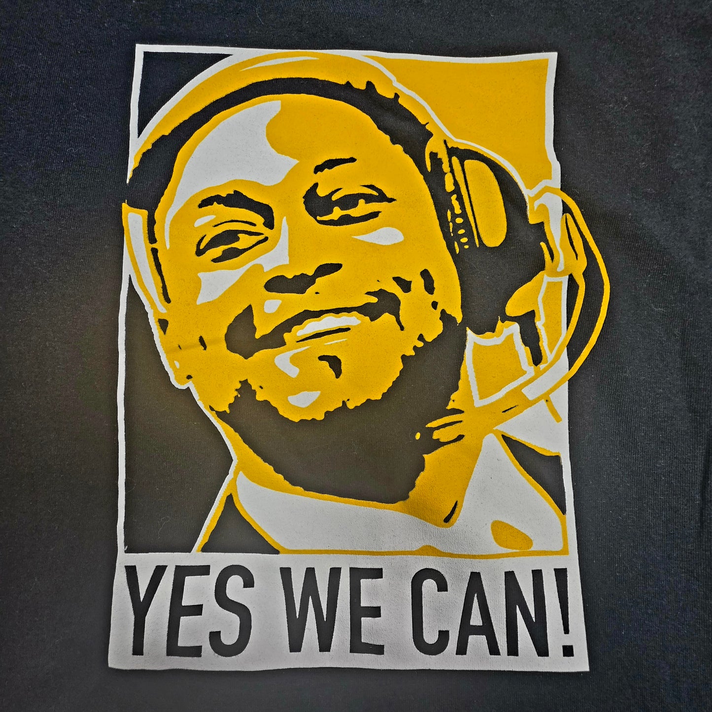 Steelers stylized graphic in yellow, white, and black of Coach Mike Tomlin in headphones with the phrase "YES WE CAN"
